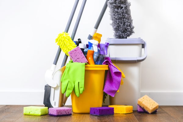 Cleaning products, household chemicals bottles and sprays, rags, sponges in orange bucket for washing the floor, brushes, broom for wiping and dusting