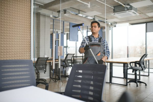 Male janitor cleaning window in office.