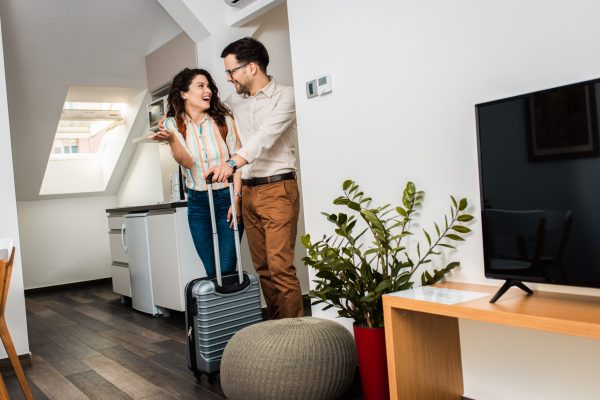 Smiling couple with suitcase arriving in hotel room.