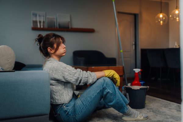 Exhausted woman wearing yellow cleaning gloves resting on living room floor, taking a break from chores